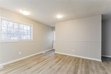Spare room with a textured ceiling, light wood-type flooring, and a wainscoted wall