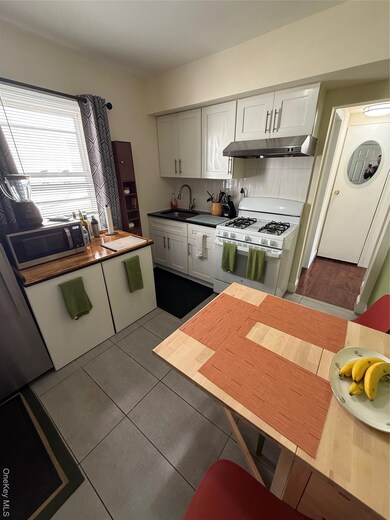 Kitchen featuring black electric range oven, ventilation hood, dark tile patterned flooring, white cabinets, and backsplash