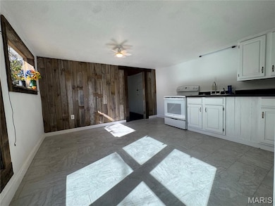 Kitchen with wooden walls, white electric range oven, dark countertops, ceiling fan, and a textured ceiling
