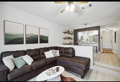 Step down into the spacious living room, featuring an open-concept design, natural light, and direct sightlines to the kitchen and dining area. Neutral finishes, laminate wood flooring, and updated lighting make this space move-in ready.