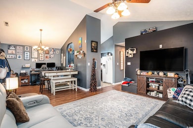 Living area with wood finished floors, ceiling fan, a chandelier, a desk, and high vaulted ceiling