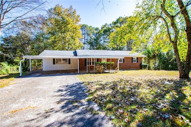 Single story home featuring asphalt driveway, an attached carport, board and batten siding, brick siding, and view of scattered trees