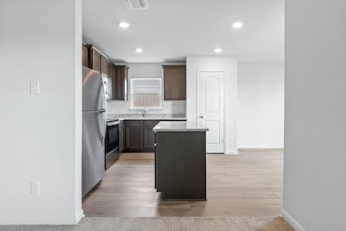 Kitchen with a kitchen island, stainless steel appliances, dark brown cabinets, recessed lighting, and light wood finished floors