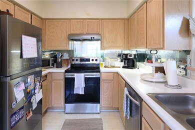 Kitchen featuring stainless steel appliances, light countertops, light brown cabinetry, and under cabinet range hood