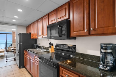 Kitchen featuring light tile patterned floors, dark stone countertops, a paneled ceiling, black appliances, and a sink