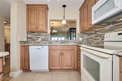 Kitchen featuring glass tile back splash, wood cabinetry, under-mount sink, tile floors. Kitchen opens to the main area of the home.
