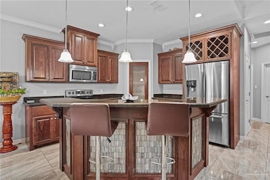 Kitchen featuring stainless steel appliances, a breakfast bar area, ornamental molding, pendant lighting, and a center island