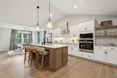 Kitchen featuring stainless steel oven, wall chimney exhaust hood, a breakfast bar, white cabinetry, and freestanding refrigerator