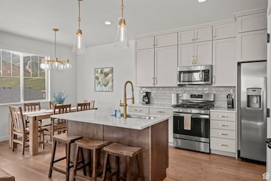 Kitchen featuring appliances with stainless steel finishes, decorative backsplash, a center island with sink, light wood-type flooring, and a breakfast bar area