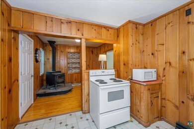 Kitchen featuring white appliances, wood walls, a wood stove, and brown cabinets