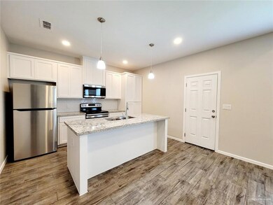 Kitchen featuring appliances with stainless steel finishes, decorative backsplash, hanging light fixtures, white cabinetry, and a center island with sink