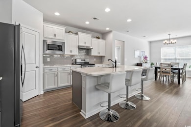 Kitchen featuring stainless steel appliances, an island with sink, white cabinets, decorative backsplash, and recessed lighting