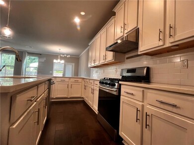 Kitchen with stainless steel gas range, under cabinet range hood, a peninsula, light countertops, and a sink