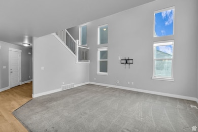 Unfurnished living room featuring a towering ceiling, light carpet, and light wood-style flooring