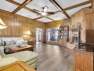 Living room featuring dark wood-type flooring, coffered ceiling, wood walls, a brick fireplace, and ceiling fan