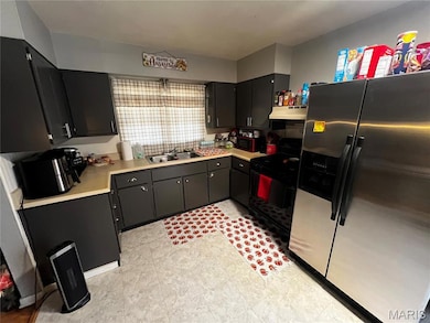 Kitchen with stainless steel fridge with ice dispenser, light countertops, black range with gas stovetop, dark cabinetry, and under cabinet range hood