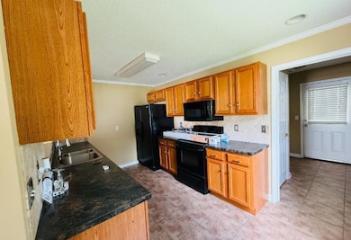 Kitchen featuring crown molding, black appliances, brown cabinets, dark countertops, and backsplash