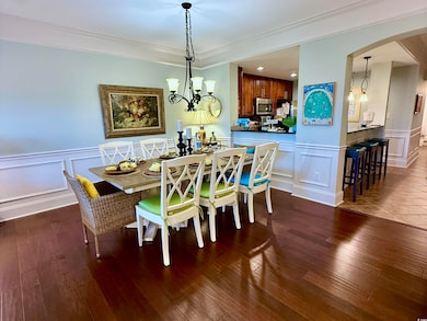 Dining area with a decorative wall, arched walkways, a wainscoted wall, wood finished floors, and crown molding