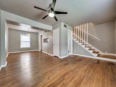 Unfurnished living room featuring wood-type flooring, ceiling fan, stairway, and a chandelier