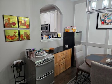 Kitchen featuring stainless steel appliances, arched walkways, dark wood-style floors, white cabinets, and decorative backsplash