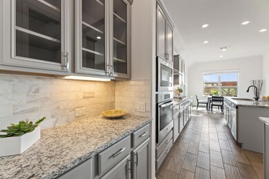 Kitchen with stainless steel appliances, a sink, gray cabinets, glass insert cabinets, and recessed lighting