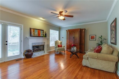 Large Family Room with a fireplace, hardwood floors, ceiling fan, crown molding, door to patio