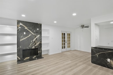 Unfurnished living room featuring recessed lighting, light wood-style flooring, french doors, a fireplace, and built in shelves