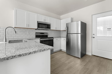 Kitchen with stainless steel appliances, white cabinets, decorative backsplash, and light stone counters
