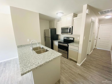 Kitchen with stainless steel appliances, a peninsula, light wood-type flooring, and light stone counters