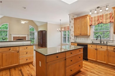Kitchen featuring black dishwasher, a sink, light wood-style flooring, a ceiling fan, and lofted ceiling