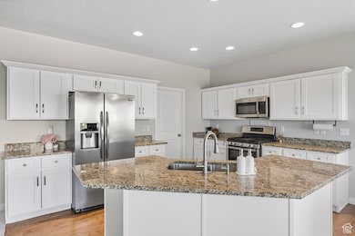 Kitchen with white cabinets, light wood finished floors, stainless steel appliances, an island with sink, and light stone countertops