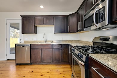 Kitchen with stainless steel appliances, dark brown cabinetry, light wood-type flooring, and recessed lighting