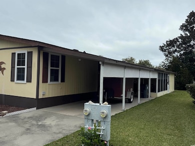 View of side of property with an attached carport, concrete driveway, a lawn, a sunroom, and a patio