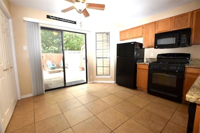 Kitchen with black appliances, a ceiling fan, light stone countertops, light tile patterned floors, and baseboards