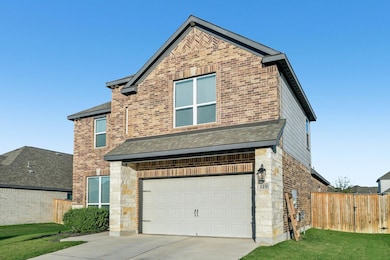 View of front of house with brick siding, roof with shingles, an attached garage, driveway, and stone siding