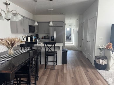 Kitchen featuring gray cabinets, stainless steel refrigerator with ice dispenser, a peninsula, a kitchen breakfast bar, and hanging light fixtures