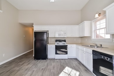 Kitchen with sink, black appliances, white cabinetry, and light wood-type flooring