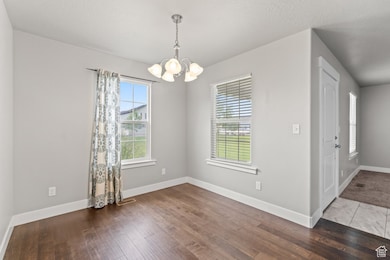 Unfurnished dining area featuring dark wood-style flooring, a chandelier, and a textured ceiling