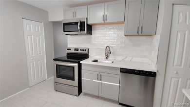 Kitchen with gray cabinetry, appliances with stainless steel finishes, backsplash, and light stone counters