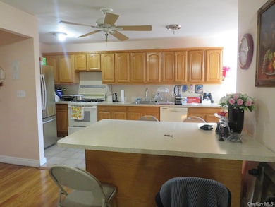 Kitchen featuring a peninsula, a breakfast bar area, white appliances, light countertops, and light wood-type flooring