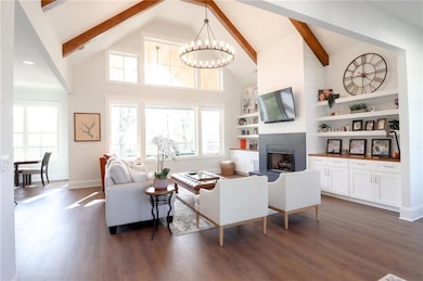 Living area with a chandelier, dark wood-style floors, high vaulted ceiling, beam ceiling, and a large fireplace
