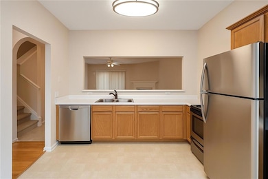 Kitchen with stainless steel appliances, light countertops, brown cabinetry, a ceiling fan, and arched walkways