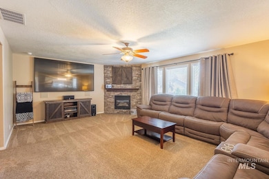 Living area featuring a ceiling fan, carpet floors, a fireplace, and a textured ceiling