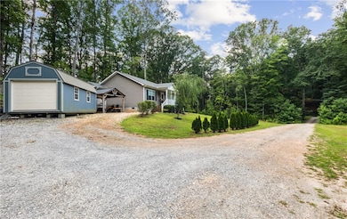 View of front of house with driveway, an outdoor structure, and view of scattered trees
