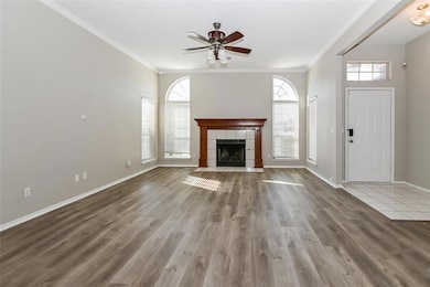 Unfurnished living room with a tile fireplace, ceiling fan, ornamental molding, and hardwood / wood-style flooring
