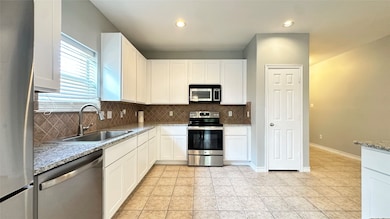 Kitchen featuring appliances with stainless steel finishes, backsplash, white cabinetry, light stone countertops, and recessed lighting