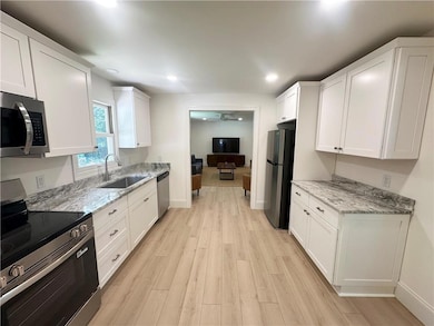 Kitchen with stainless steel appliances, light wood-style floors, ceiling fan, white cabinetry, and recessed lighting