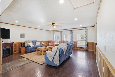 Living area featuring dark wood-type flooring, a fireplace, recessed lighting, wainscoting, and electric panel