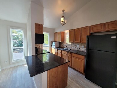 Kitchen with freestanding refrigerator, light wood-style floors, brown cabinetry, decorative backsplash, and lofted ceiling
