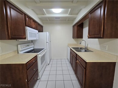 Kitchen with white appliances, dark brown cabinets, light tile patterned floors, light countertops, and beam ceiling